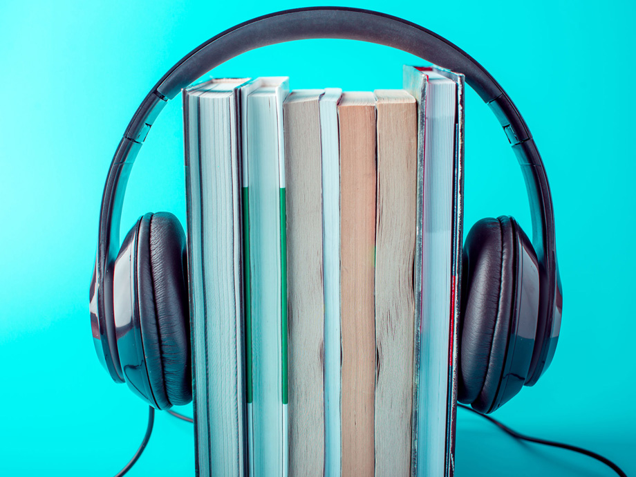 Black headphones with a stack of books on a blue background. The concept of audiobooks and modern education