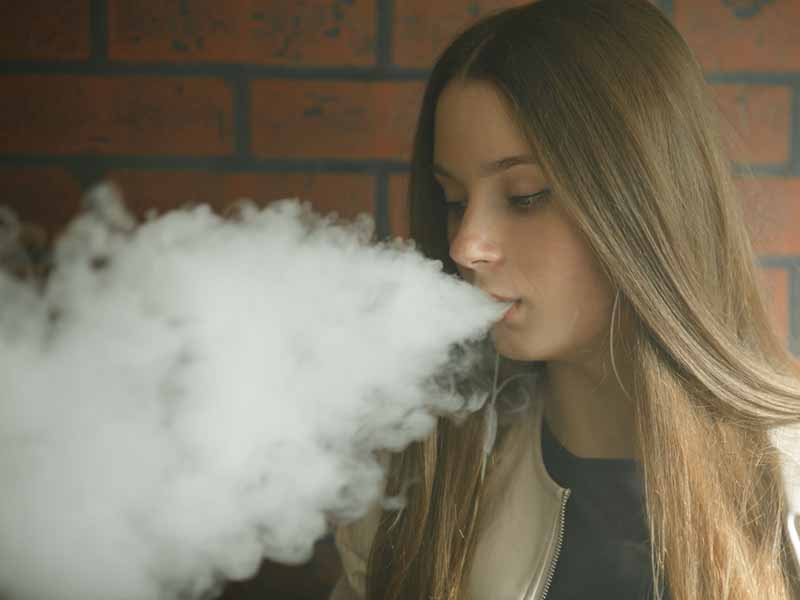 Vaping teenager. Young pretty white girl smoking an electronic cigarette in vape bar. Bad habit.