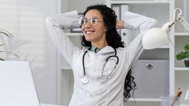 female physician smiling at desk with hands behind her head