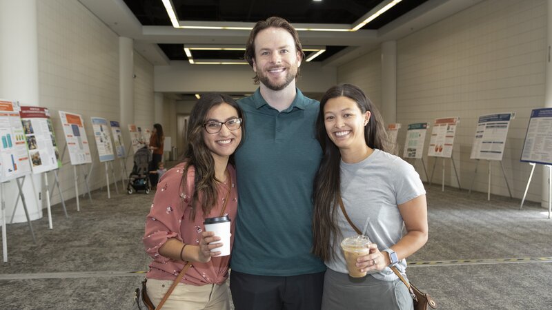 Three people smiling in a row holding coffee cups