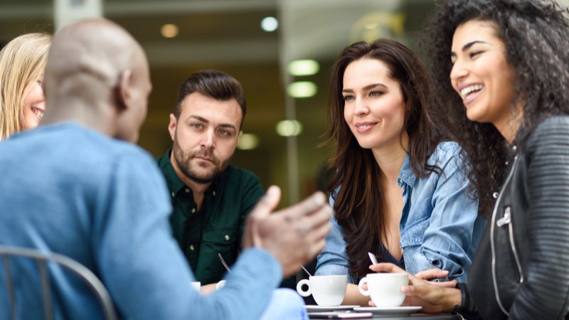 five people around table talking and smiling