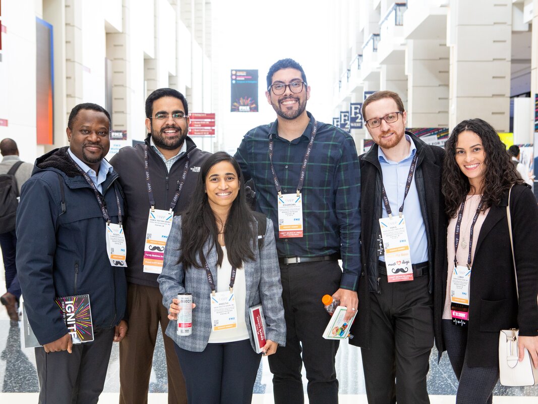 Six people smiling in a row in a convention center