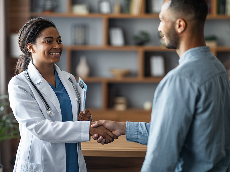 Young black woman doctor smiling shaking hands with black male patient in an office setting