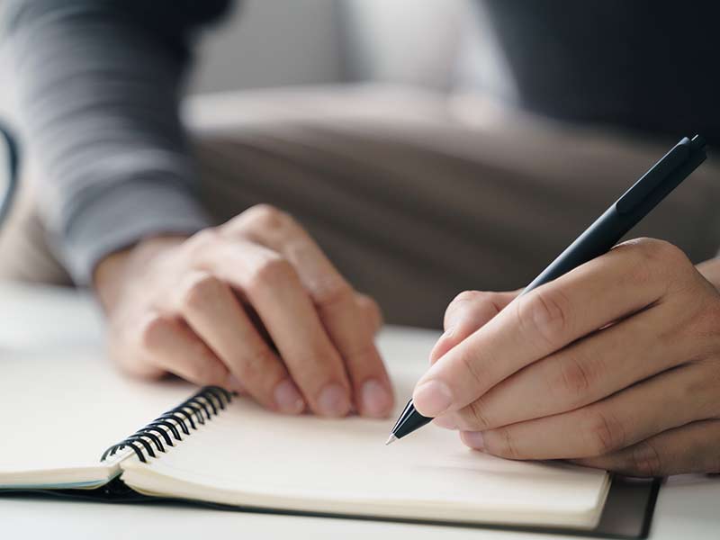 Up close of hands holding a pen writing in a notebook