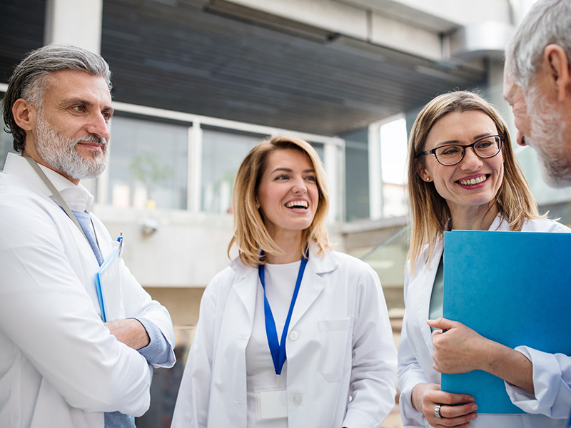 Four health care professional standing outside smiling and talking with each other