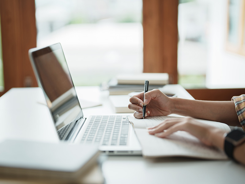 Up close of female hands holding a pen with notebook in front of laptop sitting at a desk