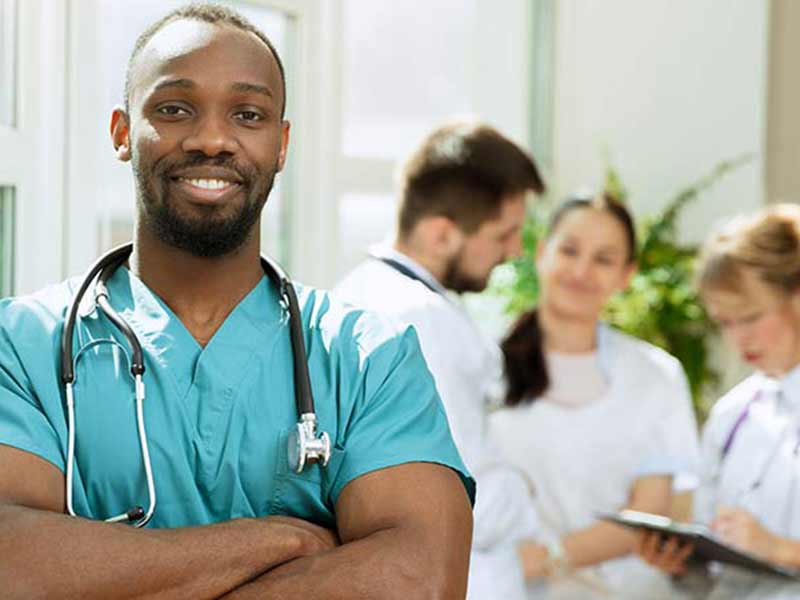 Young black healthcare professional with a stethoscope smiling with three colleagues behind him in the background