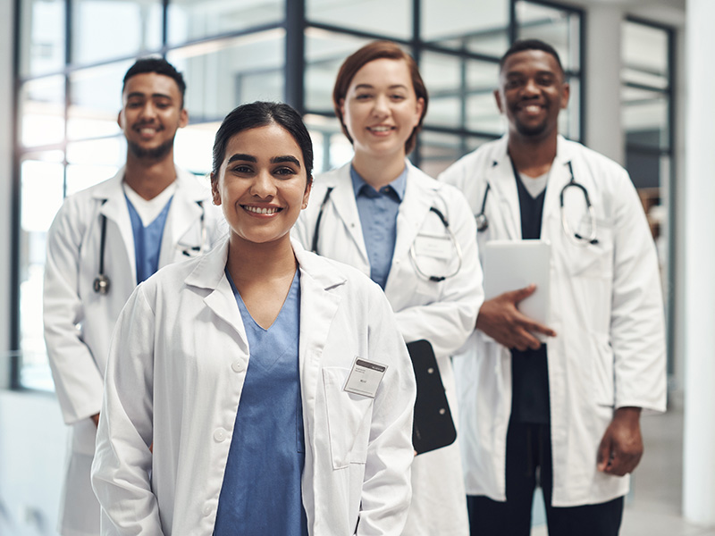 Four health care professional smiling wearing white coats standing in hallway.