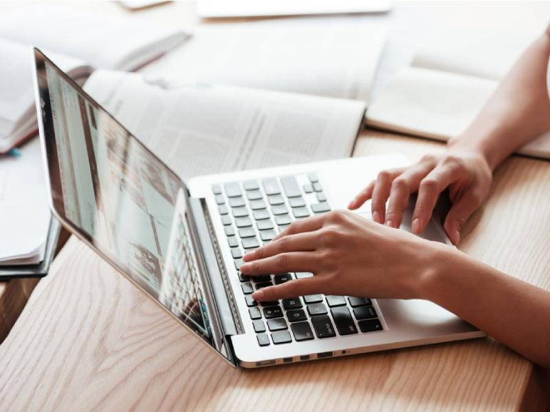 Up close of hands typing on a laptop surrounded by text books