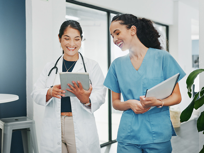 Female doctor and nurse smiling standing in a hallway looking at documents