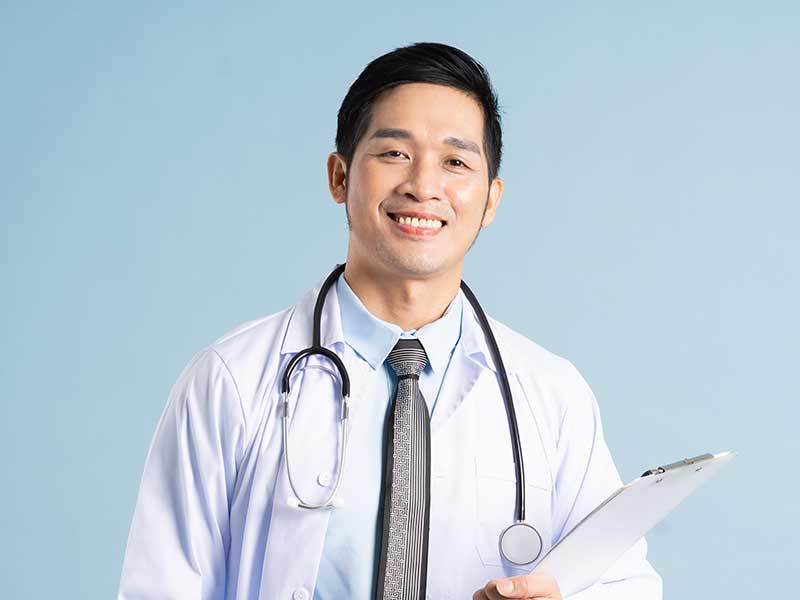 Young Asian man dressed with a tie and white coat with a stethoscope around his neck smiling