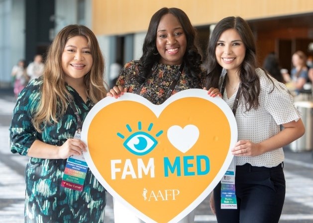 Three women in a row holding a sign in the shape of a heart that says I heart Fam Med and the AAFP logo below it.