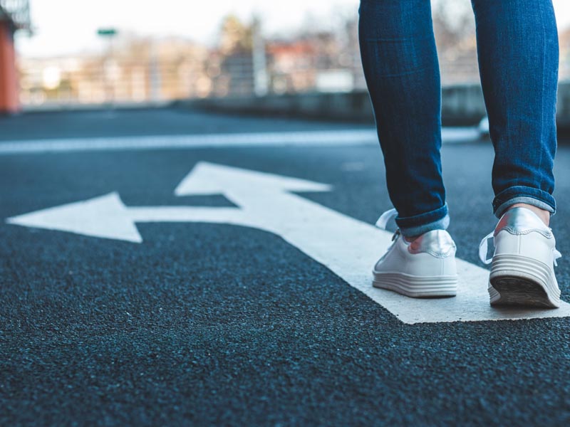 Image of shoes walking on street with arrows pointing straight and to the left. 