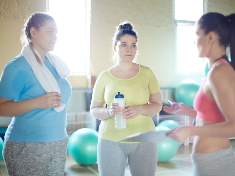 Two teens in gym talking with trainer.