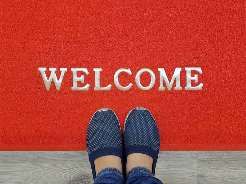 Red mat that says Welcome with two shoes showing under the word