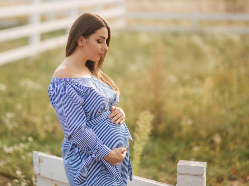 Woman holding and looking down at pregnancy belly outside in grass field